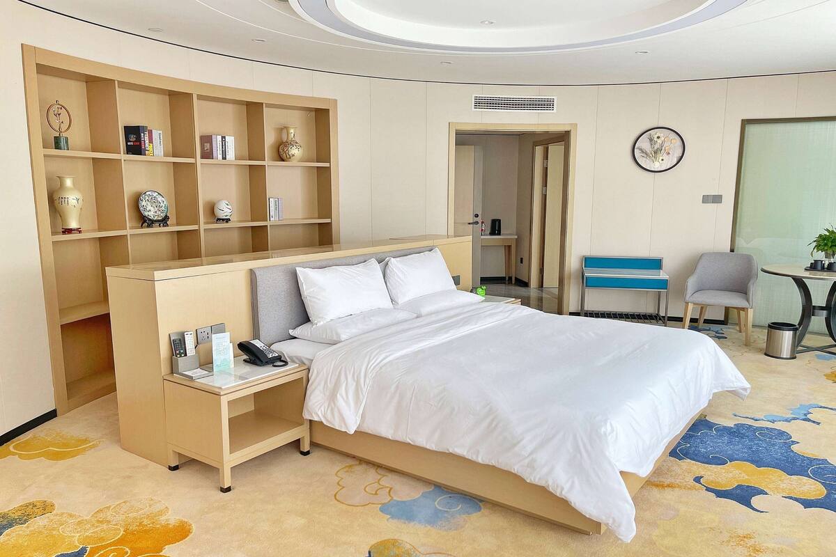 Una habitación de hotel con una cama, un escritorio con teléfono, una estantería y una silla.