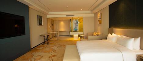 A modern hotel room with a large bed, a flat-screen TV, a desk, and a seating area.