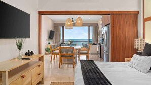 A modern hotel room with a large bed, a wooden desk, a dining area, and a view of the ocean. - Oceanfront  Condo at Costa Azul Beach ! (San José del Cabo)