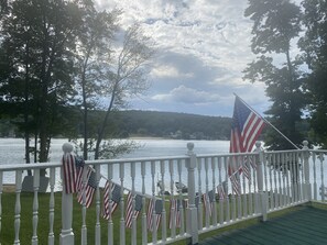 A deck with a railing overlooking a lake, adorned with American flags. - Amazing Lakefront Property (Middlefield)