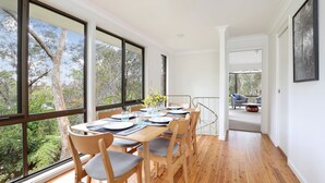 Un comedor con una mesa larga, sillas y ventanas amplias que dan vistas a árboles.