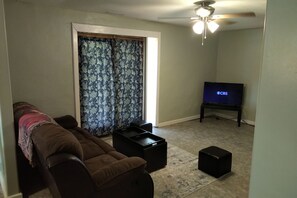 Una sala de estar con sofá, televisor sobre un mueble bajo y ventilador de techo.
