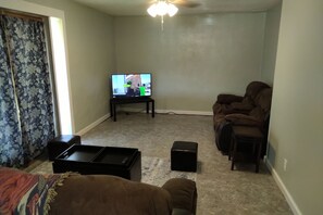 Una sala de estar con televisión, sofá, una mesa de centro y un pequeño reposapiés.