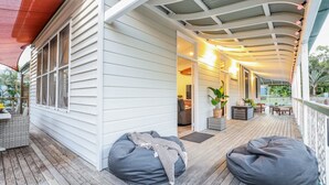 A covered porch with a wooden deck, grey bean bag chairs, and a dining area with outdoor furniture. - WESTACOMBE -  boat parking plus amazing pool, pet friendly (AGNES WATER)