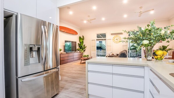 A modern kitchen with a stainless steel refrigerator, wooden flooring, and a central island with a sink.