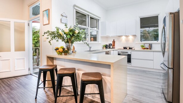 A modern kitchen with a central island, bar stools, a refrigerator, and a window overlooking a garden. - WESTACOMBE -  boat parking plus amazing pool, pet friendly (AGNES WATER)