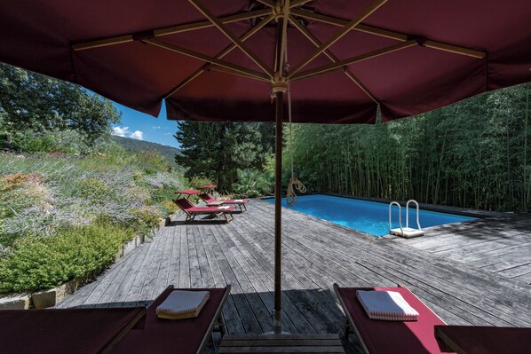 A wooden deck with a pool, red lounge chairs, and a large umbrella. - LE SCUDERIE: Villa with private pool and garden (Lubaco Pontassieve Firenze - Toscana)
