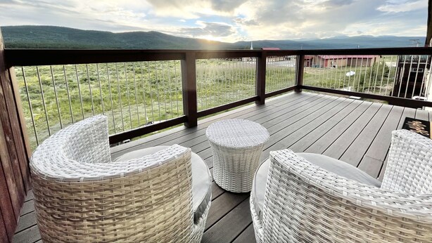 A wooden deck with wicker chairs and a view of a grassy field and mountains.
