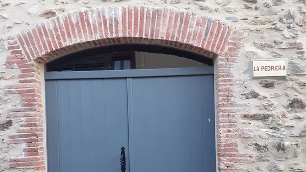 A large, closed double door with a metal handle, set within a stone wall with a brick archway above it. A sign reading "LA PEDRERA" is visible on the wall to the right of the door. - House with two terraces (espolla)