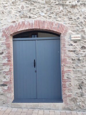 Una gran puerta doble cerrada, con un picaporte de metal, ubicada en una pared de piedra con un arco de ladrillo encima. Se observa un letrero que dice