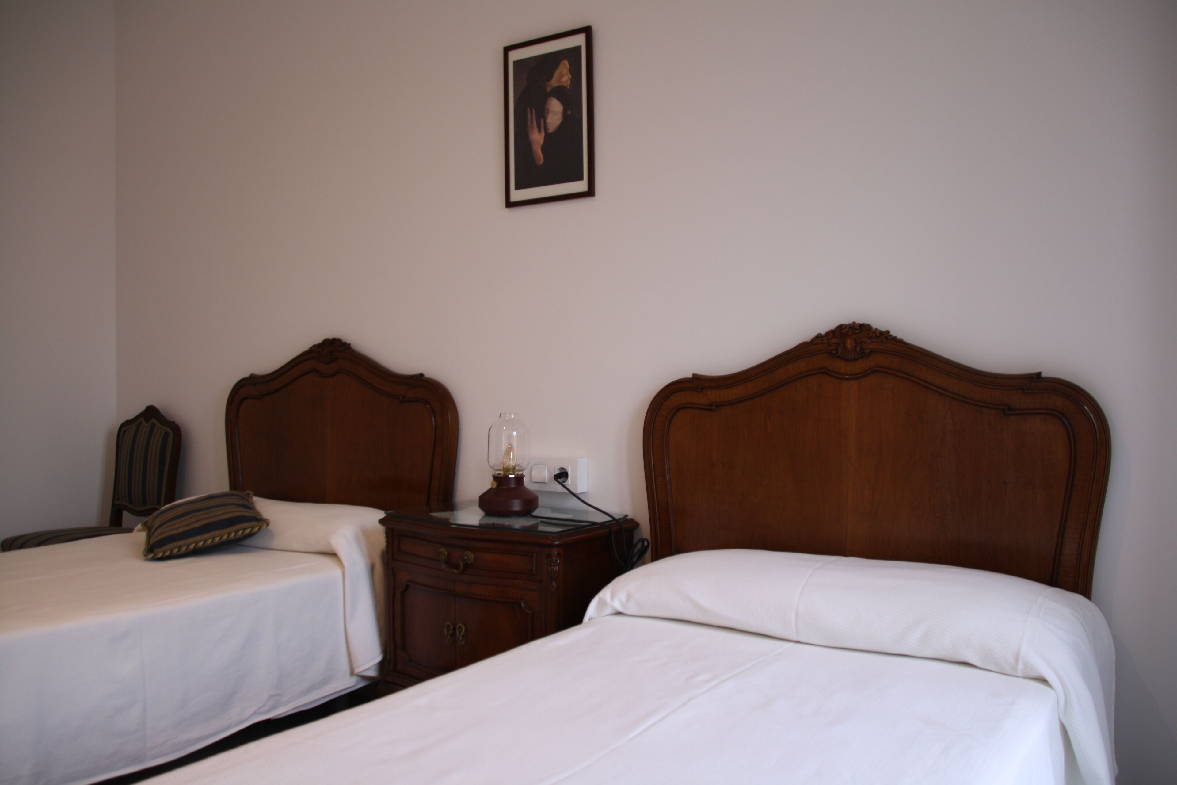 Une chambre d’hôtel avec deux lits simples, une table de chevet en bois, une lampe et un tableau encadré au mur.