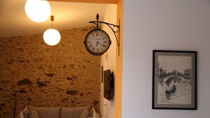 A room with a stone wall, a hanging clock, a framed picture of a bridge, a sofa, and a small table with a lamp. - House with two terraces (espolla)