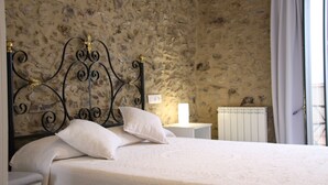 A bedroom with a stone wall, a bed with white bedding, a black metal headboard, and a bedside table with a lamp. - House with two terraces (espolla)