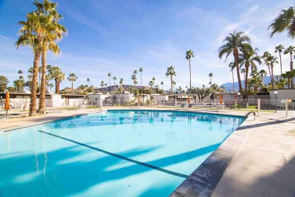 A swimming pool with clear blue water, surrounded by palm trees and a mountainous backdrop. - Mid-Century Modern Gem with a BBQ Patio (Palm Springs)