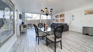Een eetgedeelte met een glazen tafel, vier stoelen, een kroonluchter en een bank.