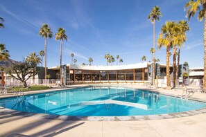 A swimming pool with a clear blue water, surrounded by palm trees and a modern building with large windows. - Mid-Century Modern Gem with a BBQ Patio (Palm Springs)
