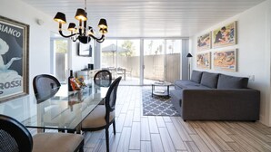 Een moderne woonkamer met een glazen eettafel, een grijze bank en een kroonluchter.
