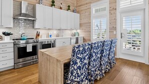 A modern kitchen with wooden paneling, white cabinets, stainless steel appliances, and a view through the window. - Enjoy Luxe Beachside Living@Cinnamon Shore Townhome w/ Great Amenities! (Port Aransas)