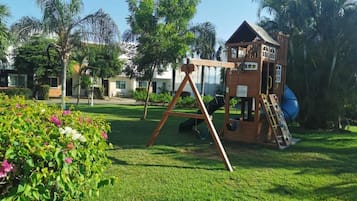 Children can play and explore in this multi-level play area with a slide, surrounded by lush greenery and mature trees.