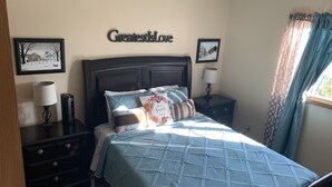 Une chambre à coucher comprenant un lit, deux tables de chevet, une commode, une lampe fixée au mur et une fenêtre avec des rideaux.