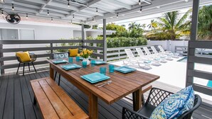 Eine Außenpatio mit Holztisch, gedeckt für ein Essen, umgeben von Liegestühlen und einem Pool.