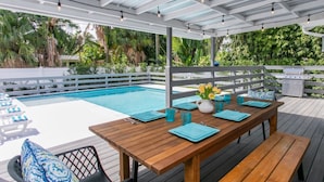 Eine Holzterrasse mit Pool, Sitzgelegenheiten und Grillplatz.