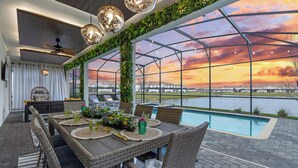 A dining area with a view of a lake and sunset, featuring wicker furniture and a pool. - Ultimate Lakeview Villa with Everything! (Kissimmee)
