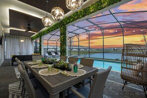 A dining area with a view of a sunset over a body of water, a pool, and outdoor seating. - Ultimate Lakeview Villa with Everything! (Kissimmee)