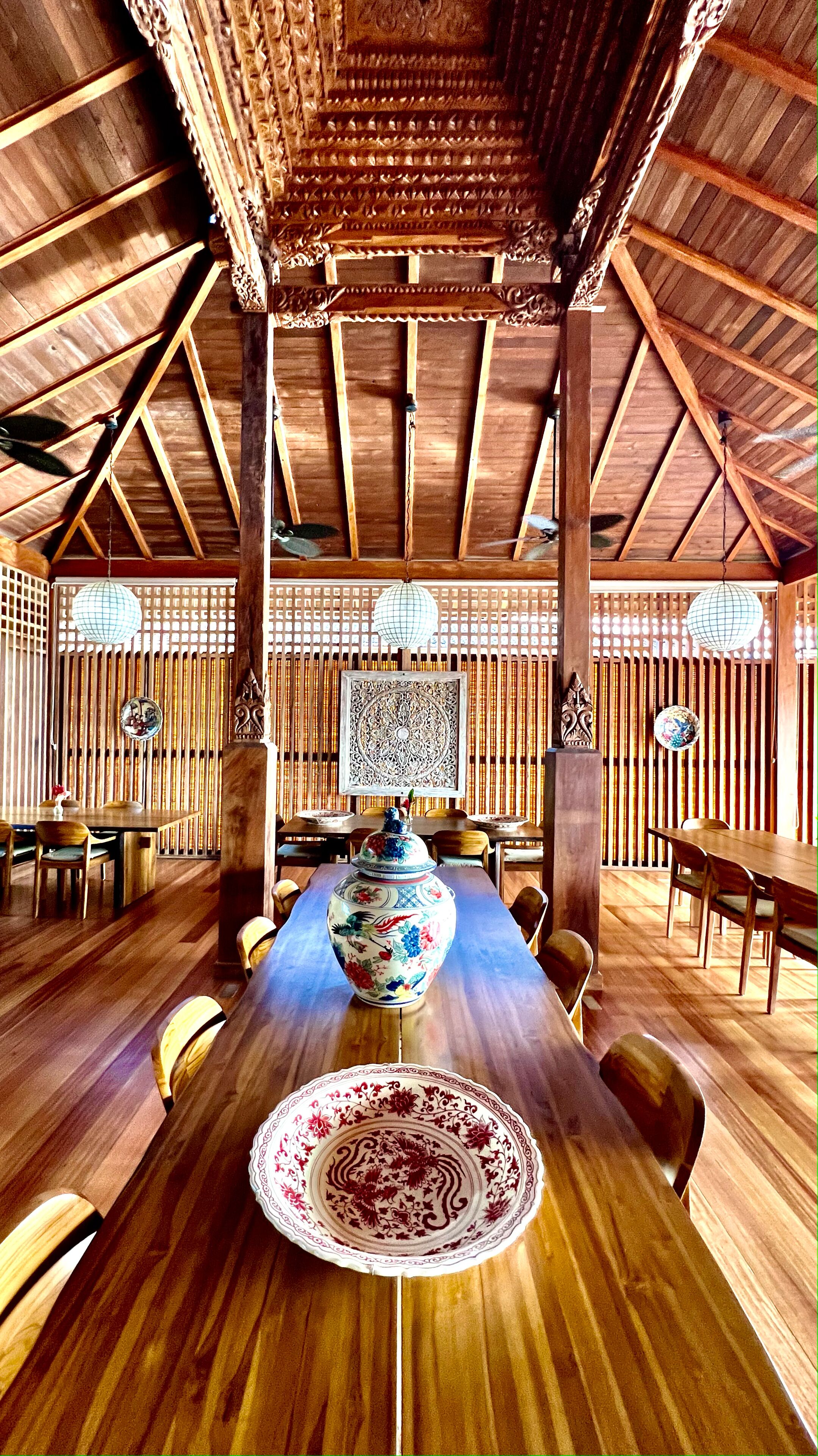 A wooden dining area with a high ceiling, wooden beams, and a large decorative vase on the table.