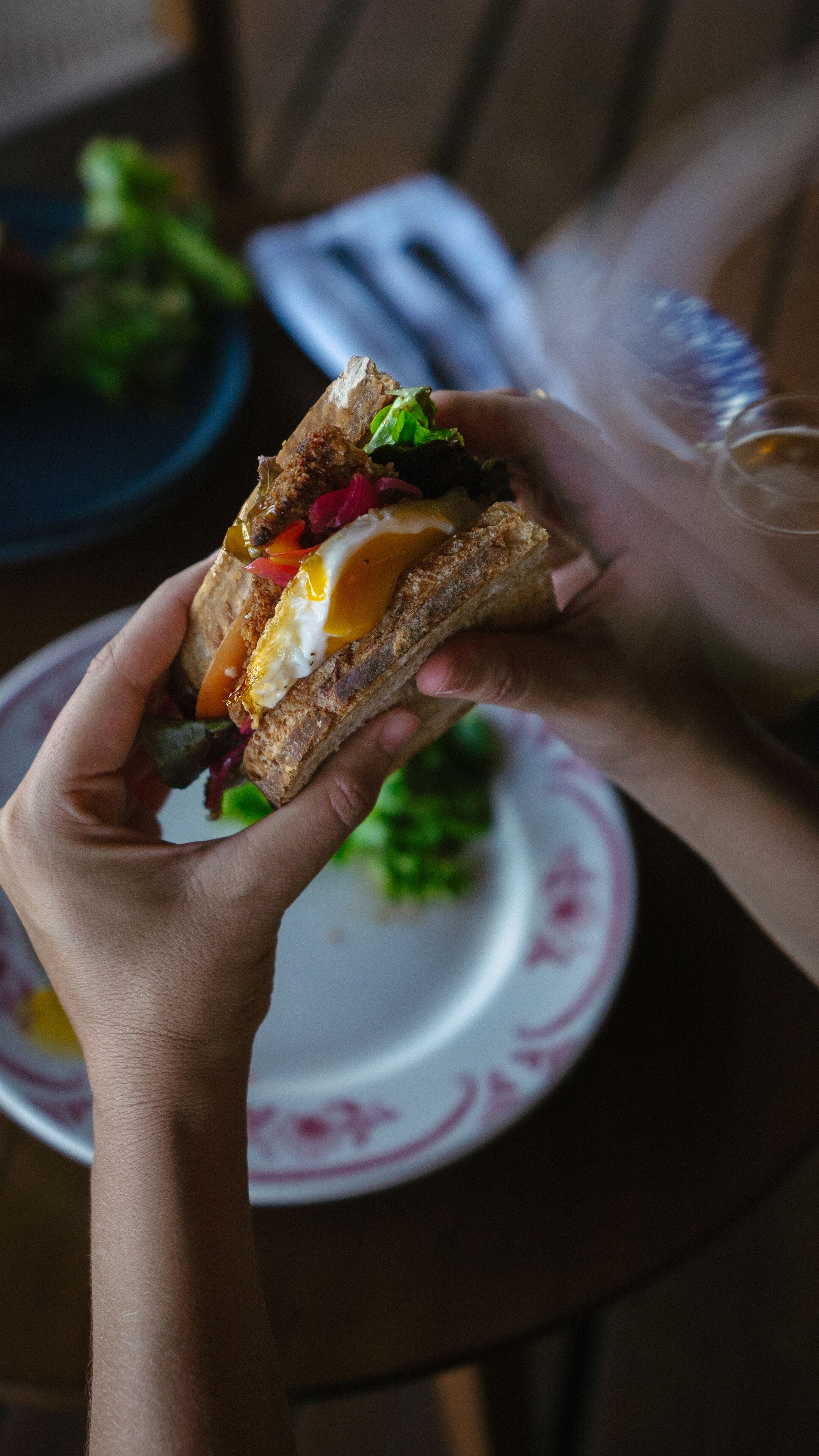 Una persona sosteniendo un sándwich con ingredientes visibles como huevo y vegetales.