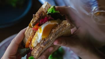 Una persona sosteniendo un sándwich con ingredientes visibles como huevo y vegetales.