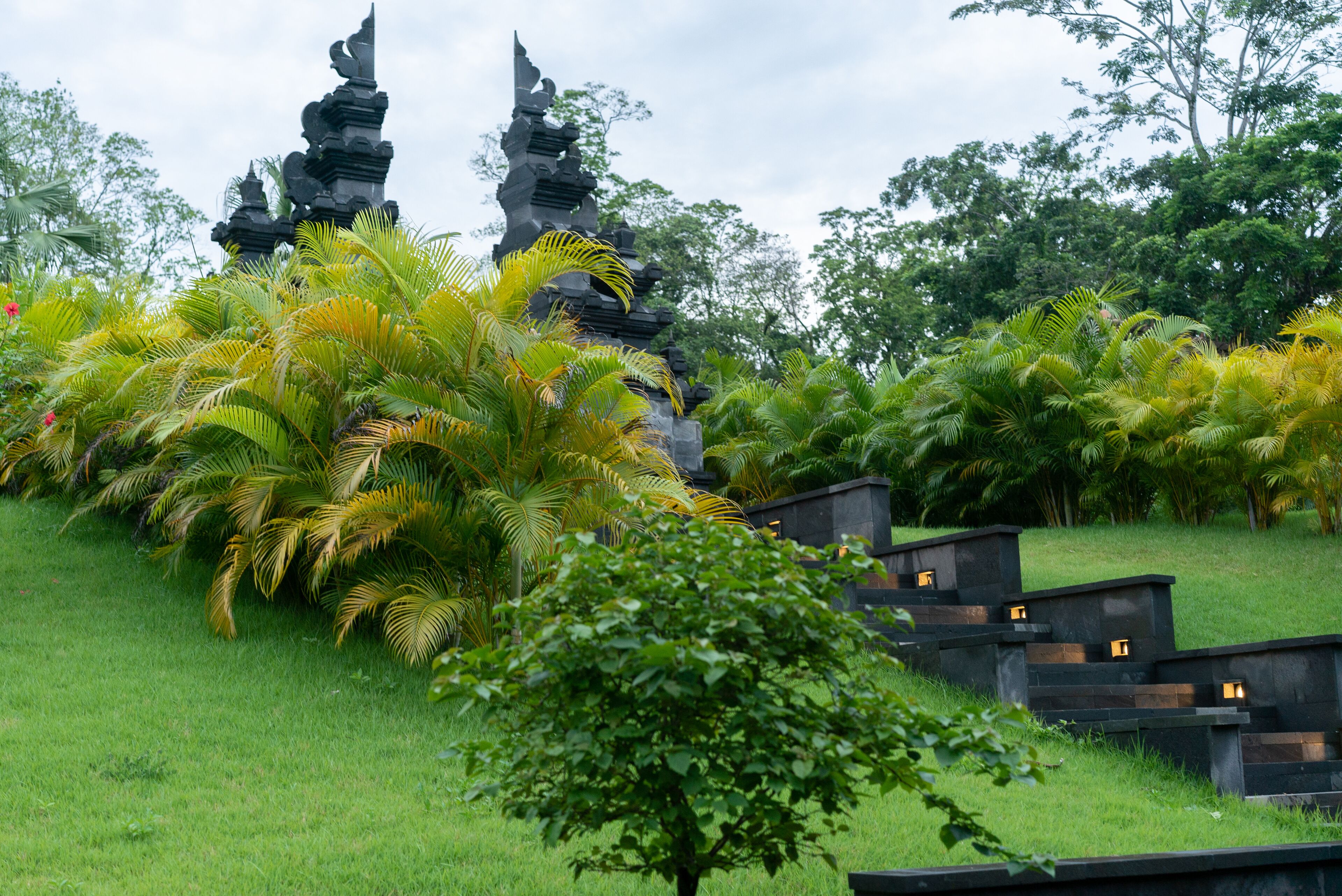 Un templo de varios niveles y un exuberante jardín verde con palmeras.