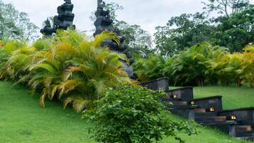 Un templo de varios niveles y un exuberante jardín verde con palmeras.