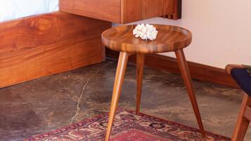 Habitación de hotel moderna con cabecera de madera, mesita de noche con un jarrón de flores rojas, un taburete pequeño de madera y una alfombra roja con estampado.