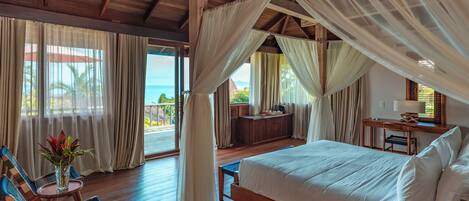 A spacious bedroom with a large bed, wooden flooring, and a balcony with curtains.