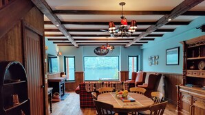 Un comedor acogedor con una mesa de madera, sillas y una araña. Se ve un lago a través de las ventanas.