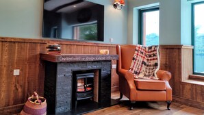 Una sala de estar acogedora con chimenea, un sillón de cuero y un televisor de pantalla plana grande montado en la pared.