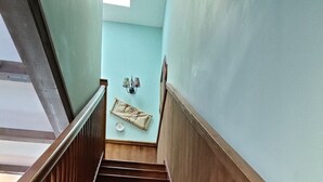 Una escalera de madera con barandilla que conduce a una plataforma con una pared azul claro y una ventana pequeña.