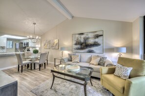 Uma sala de estar moderna com uma mesa de centro de vidro, um sofá bege e uma área de jantar com uma mesa e cadeiras de vidro.