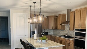 A modern kitchen with a large island, bar stools, wooden cabinets, stainless steel appliances, and pendant lighting. - 3 bedroom house with Golf, pool, hot tub, gym, biking, and much more (Buckeye)