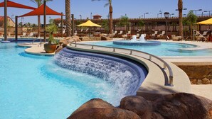 A pool with a waterfall feature, lounge chairs, and umbrellas. - 3 bedroom house with Golf, pool, hot tub, gym, biking, and much more (Buckeye)
