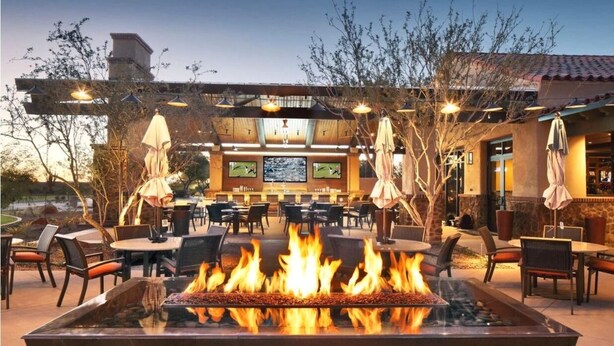 An outdoor patio area with a fire feature, dining tables, and chairs. - 3 bedroom house with Golf, pool, hot tub, gym, biking, and much more (Buckeye)