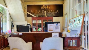 Een receptiebalie met een bordje voor Villa Daniella Beach Resort Maleisië, een computer, een printer en een prikbord met diverse objecten.