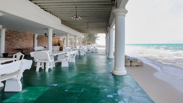 Een terras met witte tafels en stoelen, een bakstenen muur en uitzicht op het strand.