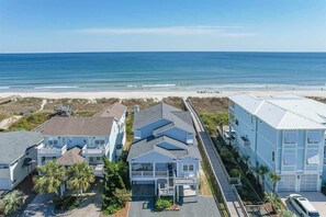 A coastal residential area with beachfront properties, including a house with a balcony and a garage. - License to Chill by Brunswick Vacation Rentals: 6BR Oceanfront w Elevator & Pool (Ocean Isle Beach)