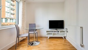 A modern living room with a glass table and chairs, a flat-screen TV, and a white entertainment unit.