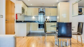 A compact kitchen with modern appliances, a dining area with two chairs, and a wooden floor.