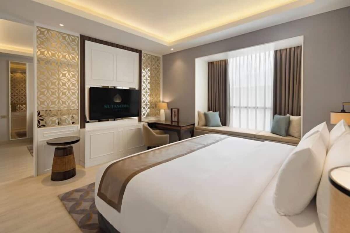 A modern hotel room with a large bed, a TV, a seating area by the window, and a decorative wall panel.