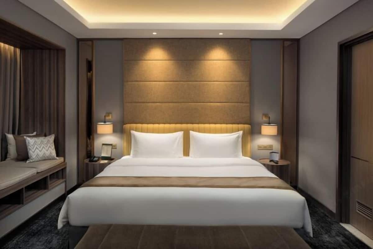 A modern hotel room with a large bed, bedside lamps, a sofa, and a wooden headboard.
