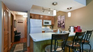 A kitchen with wooden cabinets, a white refrigerator, a microwave, and a stove. There are three bar stools and a small rug. - Welcome Inn- Pools - Great Balcony - Trails to Fishing -SO Close to Sdc!! (Branson West)
